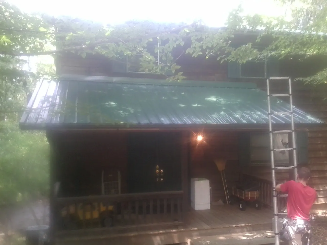Worker on a ladder at the green porch roof of a wooded cabin in Burnsville