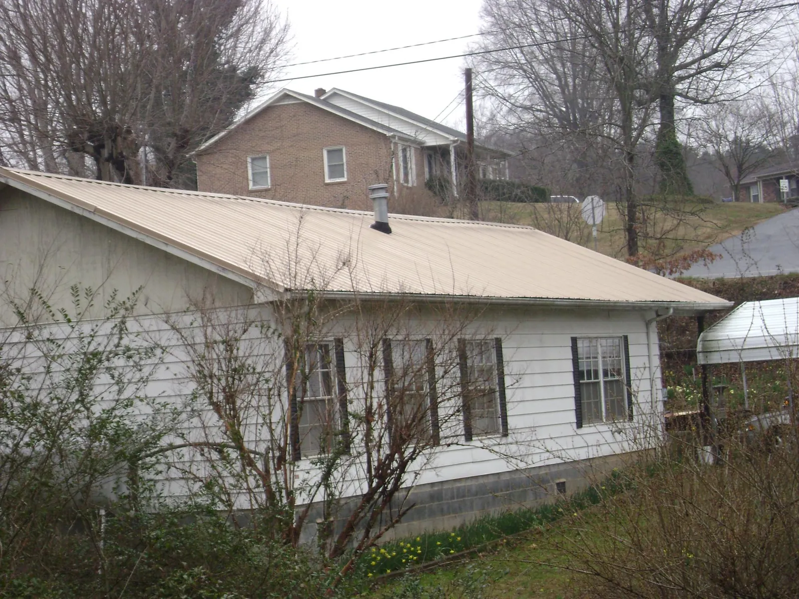 Tan metal roof on a white sided house set into a hillside — Commercial Roofing by Roofing Brothers in Burnsville